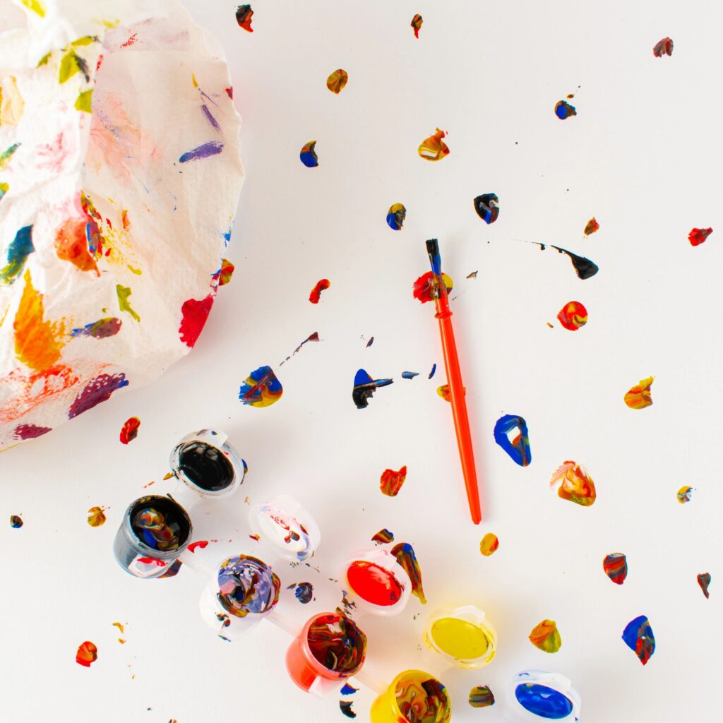 Wrinkled paper splattered with vibrant paint dots on white background. Minimal abstract idea. Flat lay. Close up.